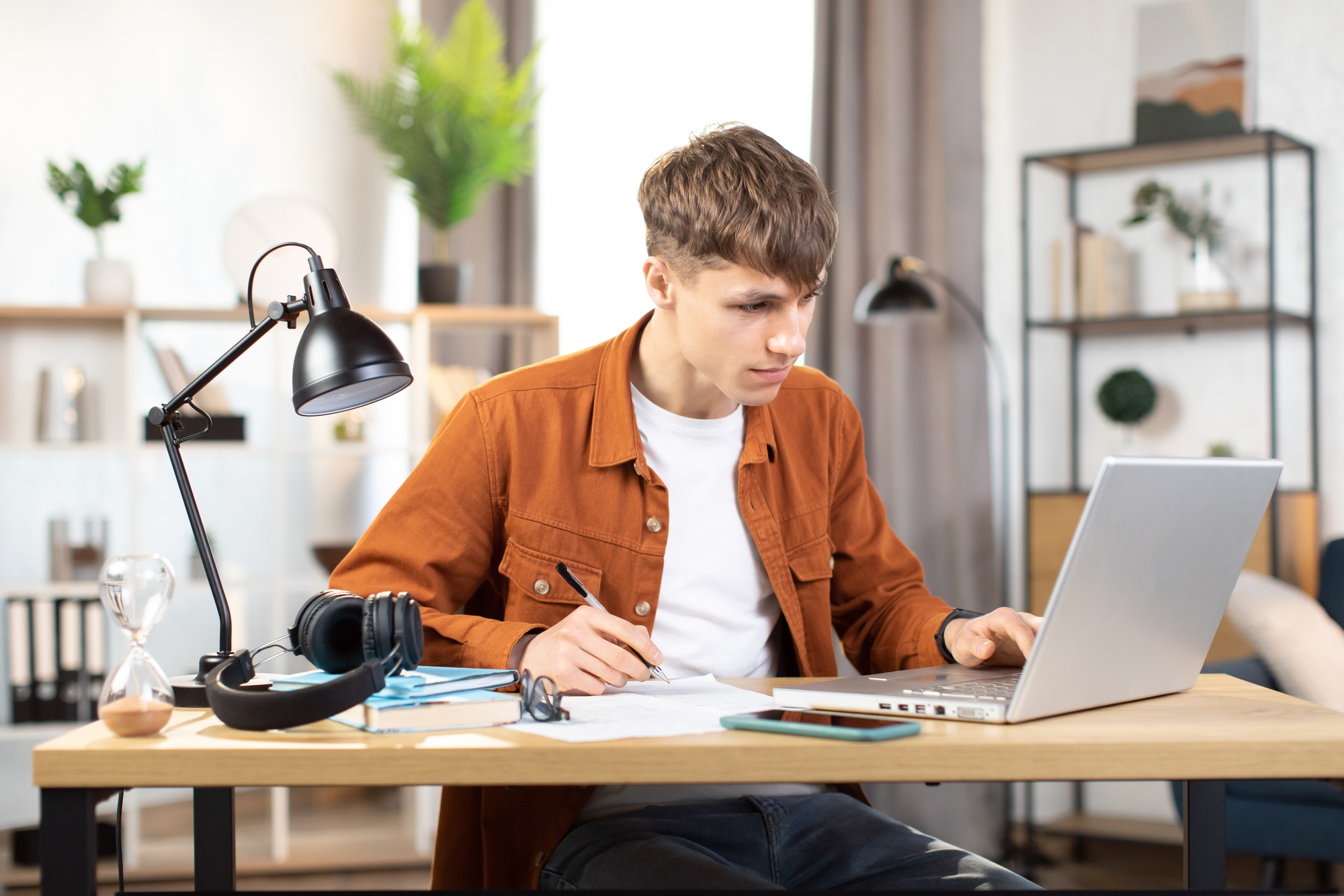 Focused young man sitting at table with laptop and making notes