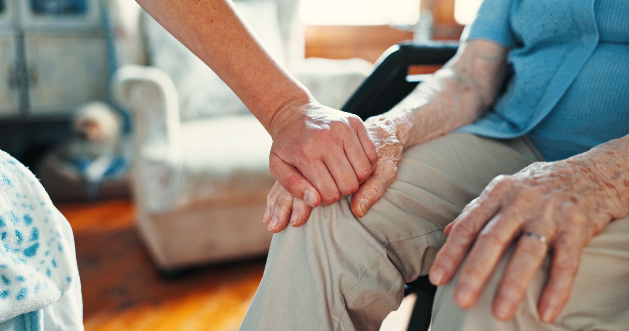 Holding hands, support and Wheelchair with old person in living room for healthcare, caregiver and